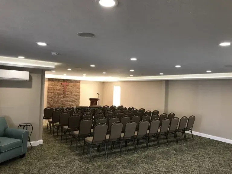 Small empty conference room with rows of chairs, a podium, and recessed ceiling lights