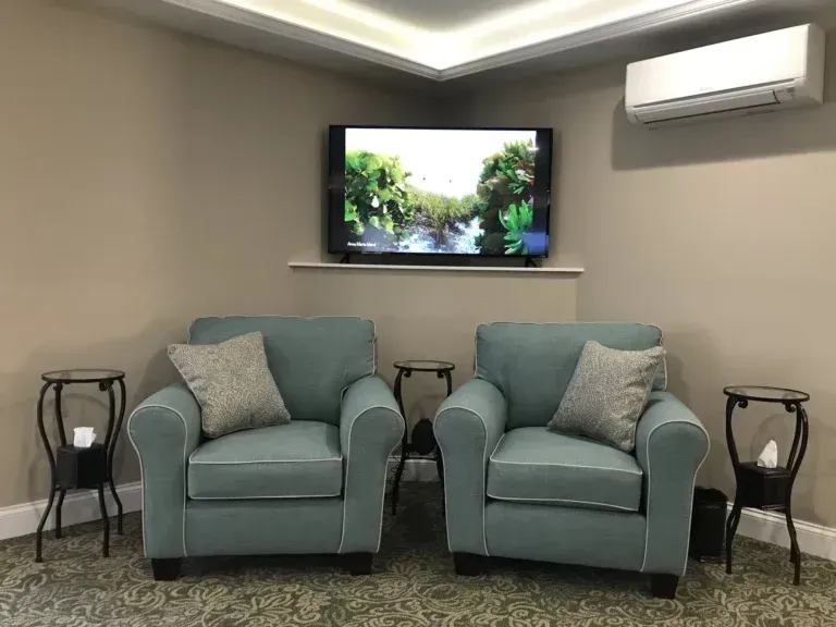 Two teal armchairs in a modern room beneath a wall-mounted TV and air conditioner