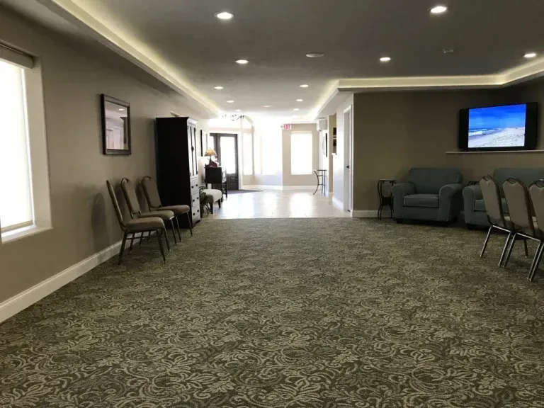 Empty hallway seating area with chairs, green couches, recessed lights, and a TV on the wall