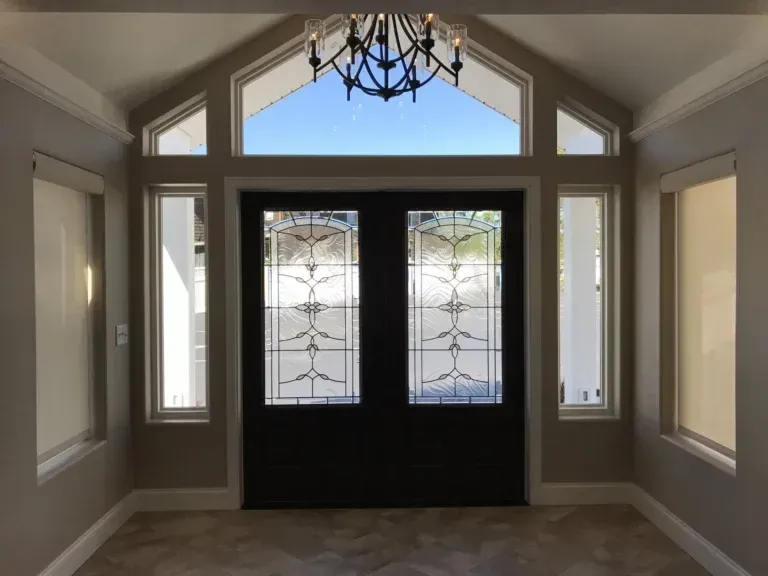 Bright entry foyer with black double doors, sidelights, and a chandelier beneath a peaked window.