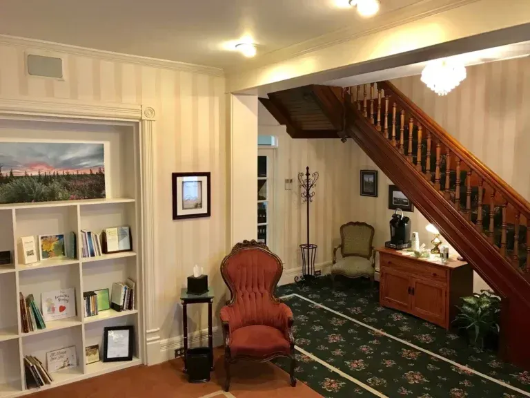 Cozy living room with bookshelf, red chair, green rug, and wooden staircase
