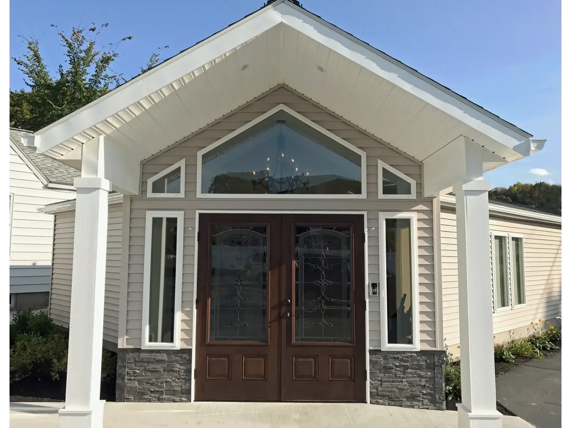 Front view of a small white house with a peaked roof, dark double doors, and large front windows