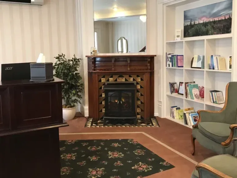 Cozy living room with fireplace, bookshelves, piano, and floral rugs in a cream-colored interior.