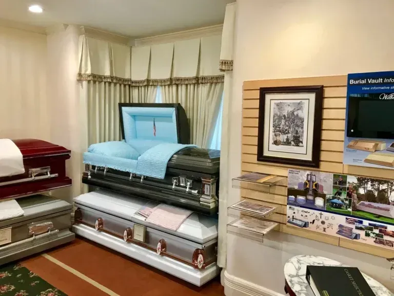 Display of funeral caskets and urns in a showroom with brochures and wall art.