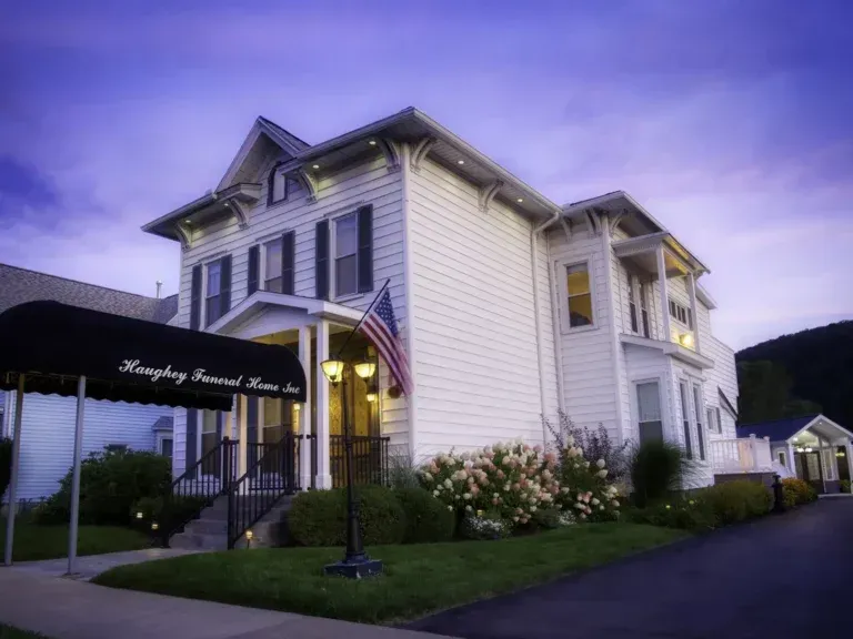White Victorian-style building with a black awning and American flag at dusk