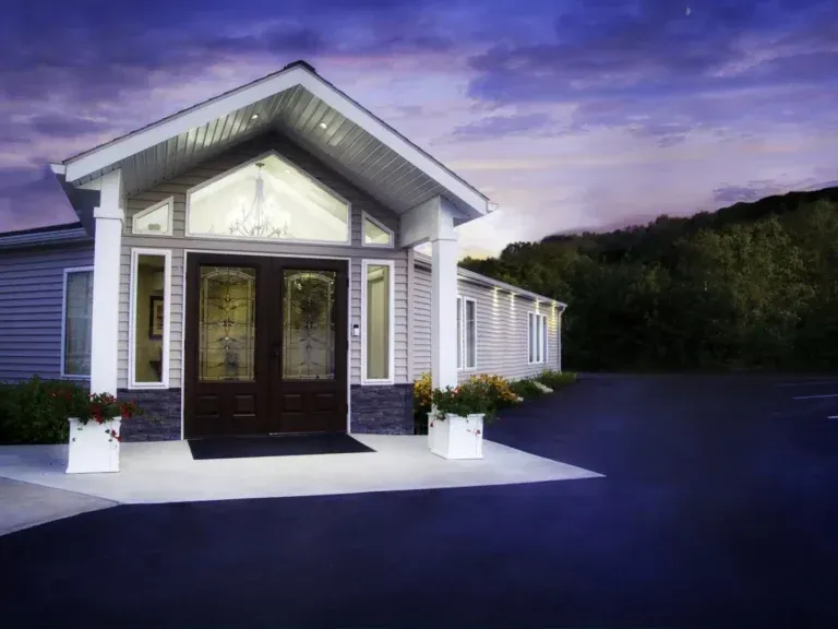 Modern white house entrance with double doors, lit porch, and potted plants at dusk