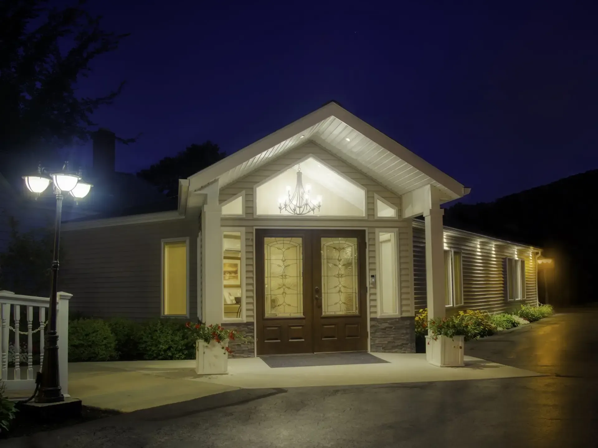 Well-lit house entrance with double wooden doors, stone columns, and porch lights at dusk