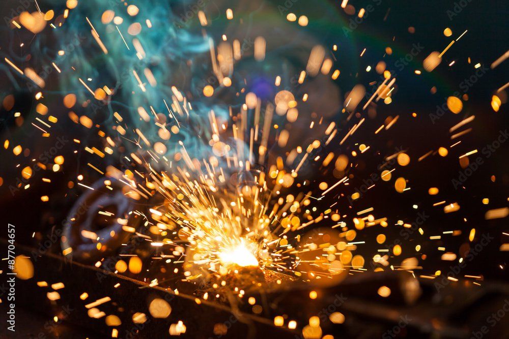 A close up of a person welding a piece of metal with sparks coming out of it.