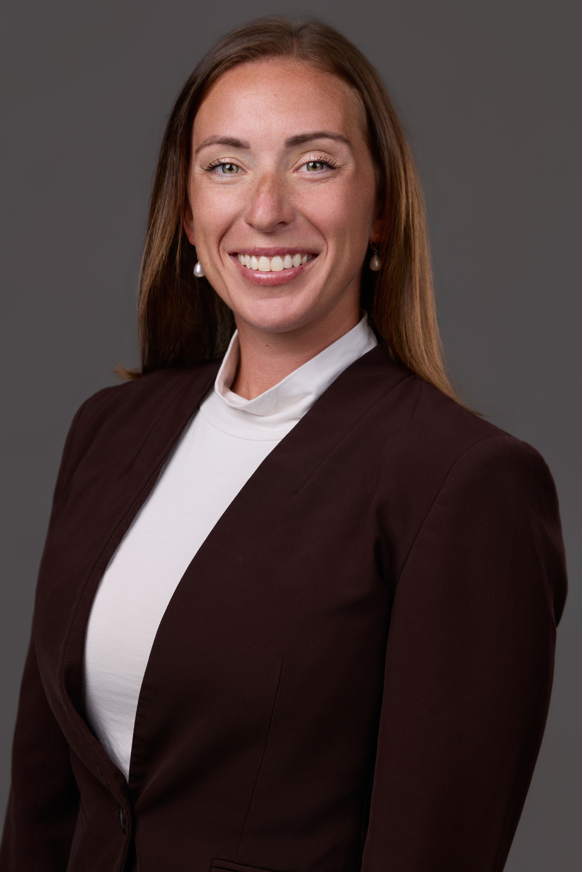 Portrait of a smiling person in a dark blazer and white top against a gray background