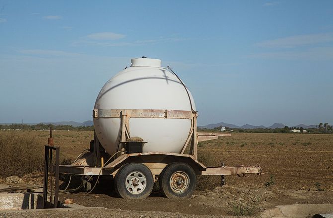 White spherical tank on a trailer in a dry field under a clear sky.