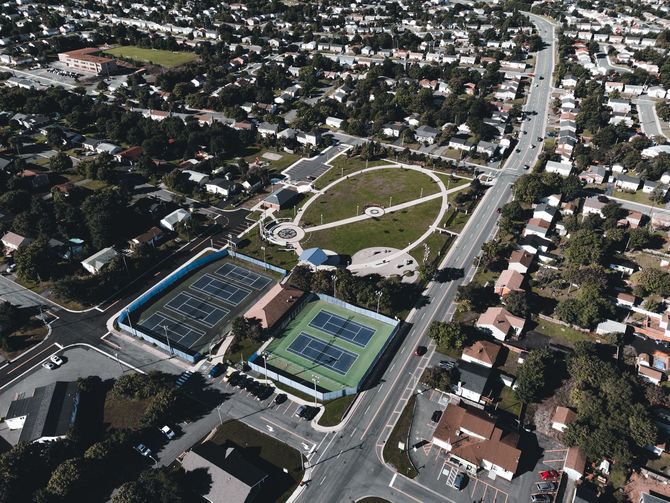 Aerial view of a neighborhood with tennis courts, a park, and intersecting roads.