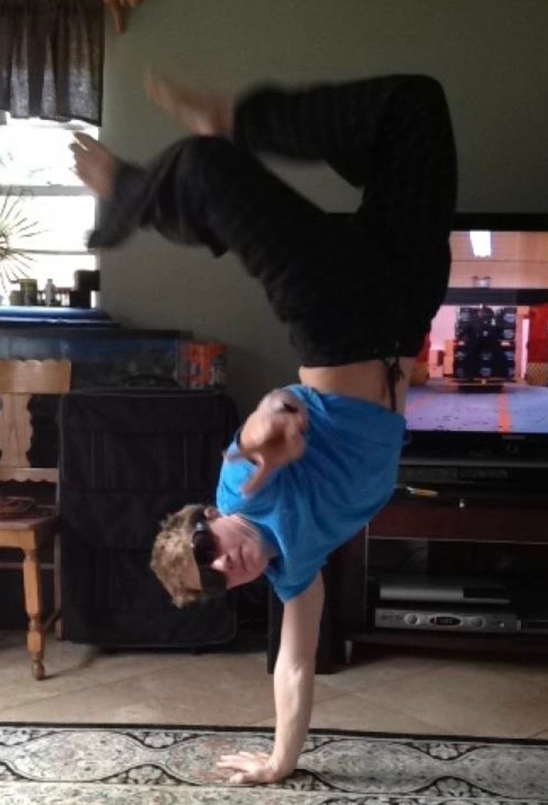 A man in a blue shirt is doing a handstand in front of a television