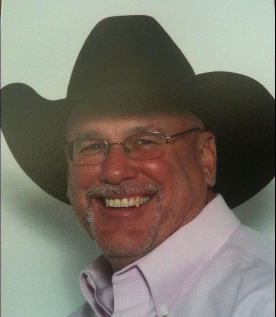 A man wearing a cowboy hat and glasses is smiling