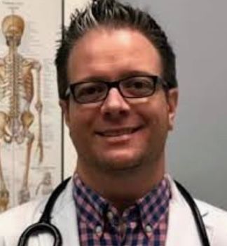 A doctor wearing glasses and a stethoscope is smiling in front of a skeleton.