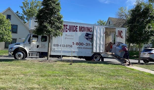 Moving truck loading furniture onto a ramp in front of a house on a sunny day.