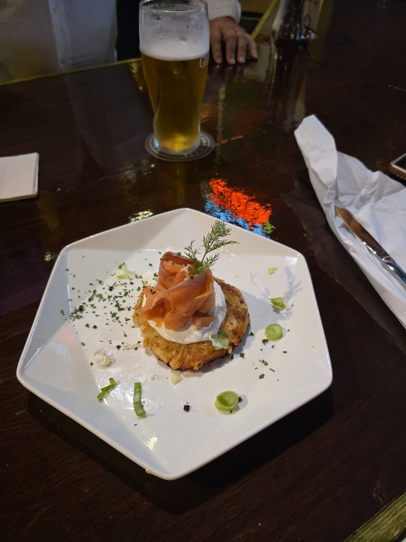Gourmet appetizer on a white plate beside a glass of beer on a dimly lit restaurant table