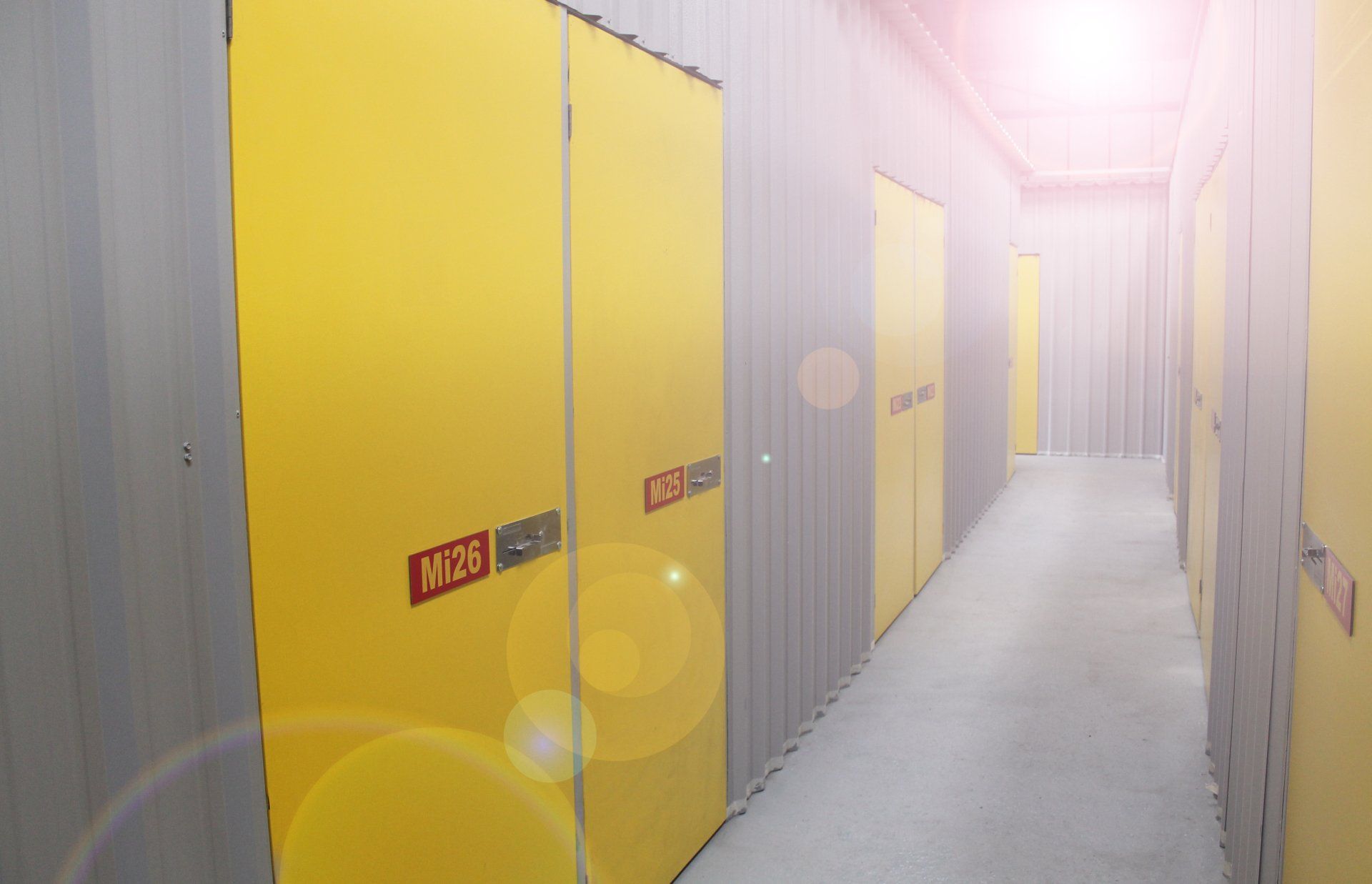 Bright yellow storage-unit doors in a narrow indoor corridor with gray doors and a white floor.
