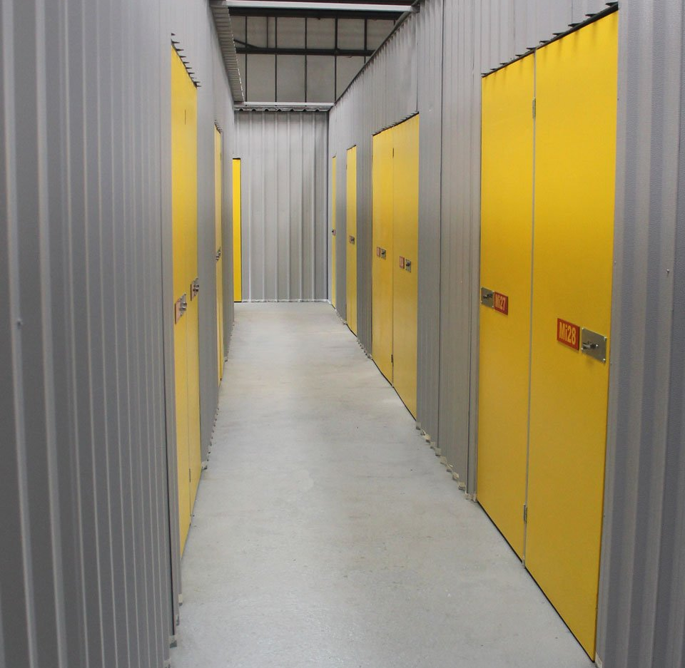 Bright yellow storage-unit doors in a narrow indoor corridor with gray doors and a white floor.