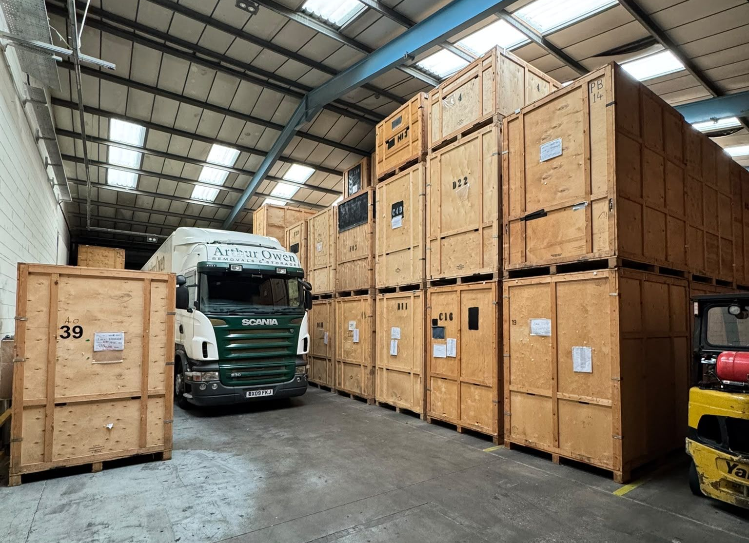 Stacked wooden shipping crates in a warehouse, numbered and arranged in rows under bright lights.