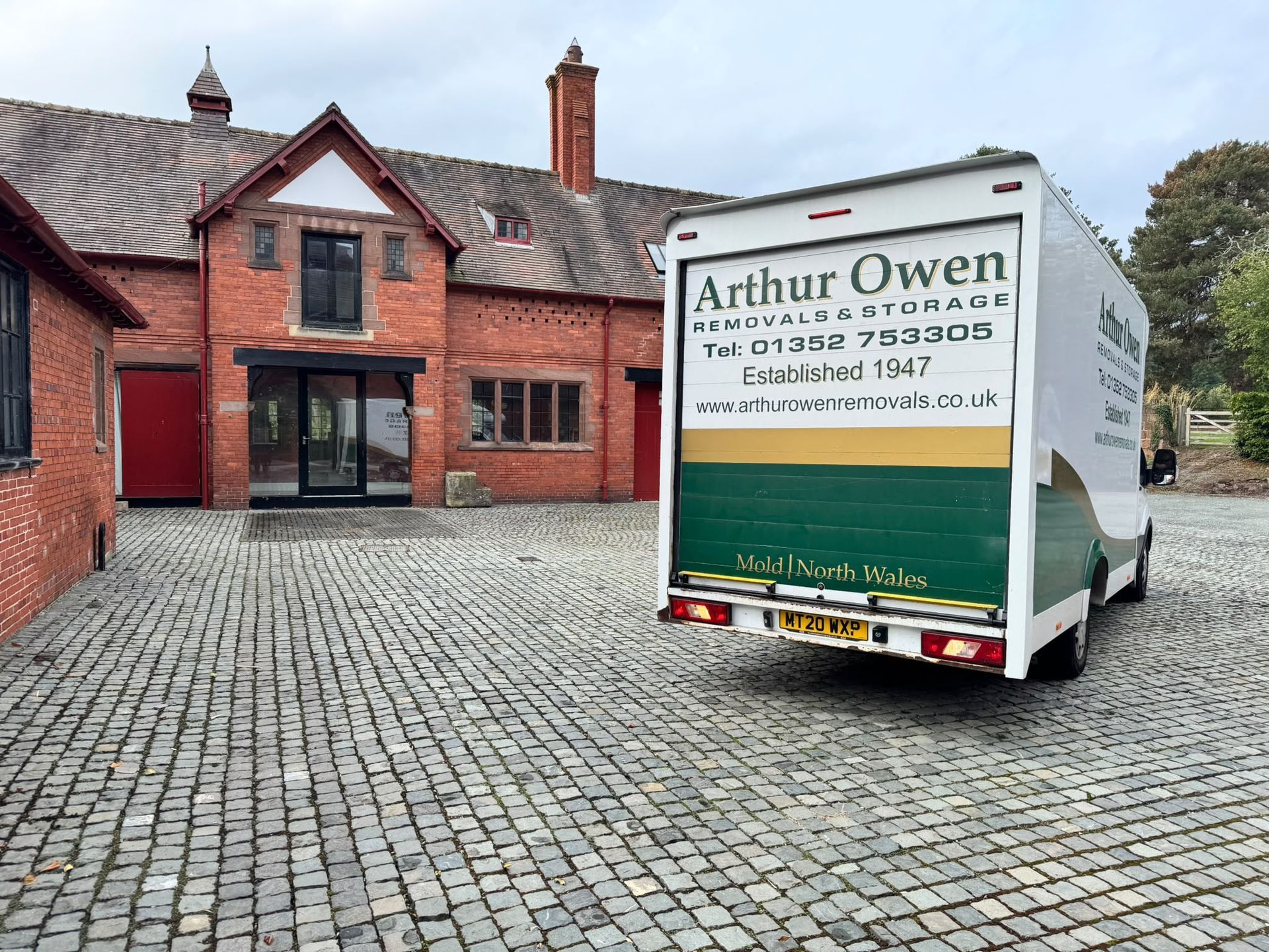Arthur Owen Removals & Storage van parked on a cobblestone driveway beside the red brick building of Eccleston Paddocks.