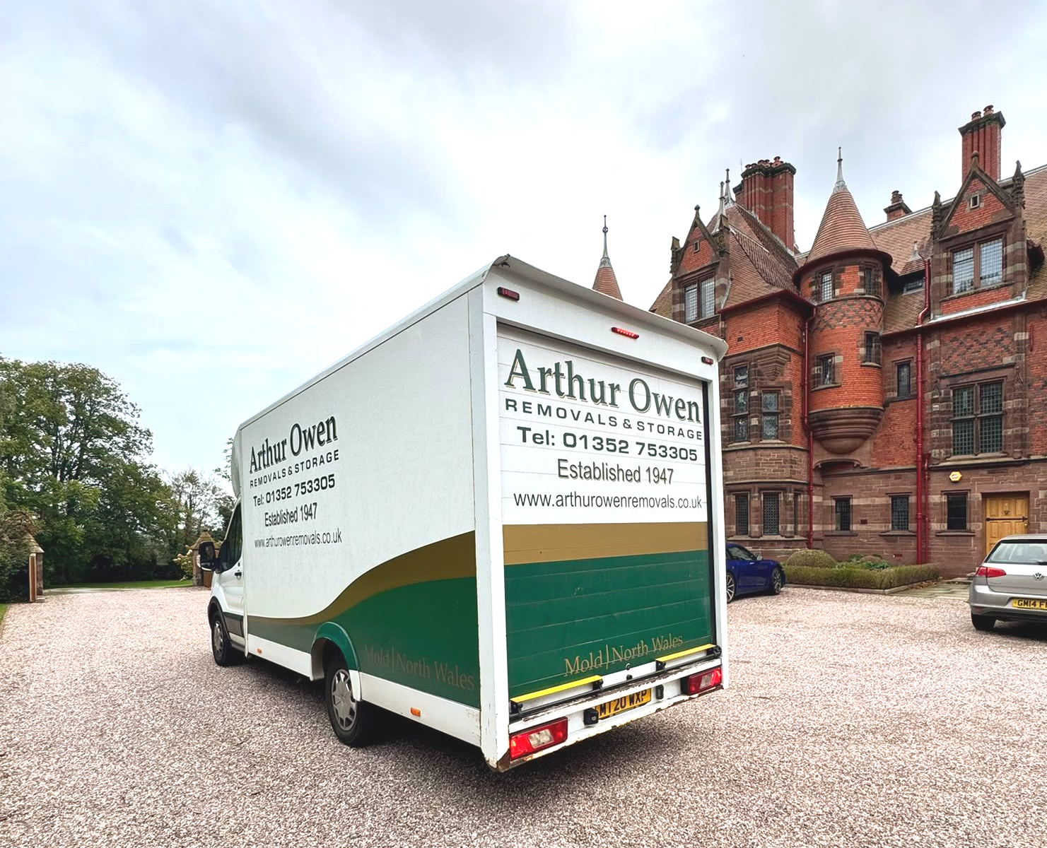 White and green Arthur Owen Removals & Storage van parked on gravel outside the red-brick building of Eccleston Paddocks.