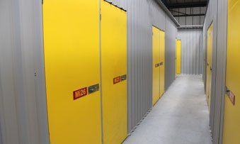 Narrow storage hallway with yellow cabinet doors and gray walls, brightly lit by overhead lights.