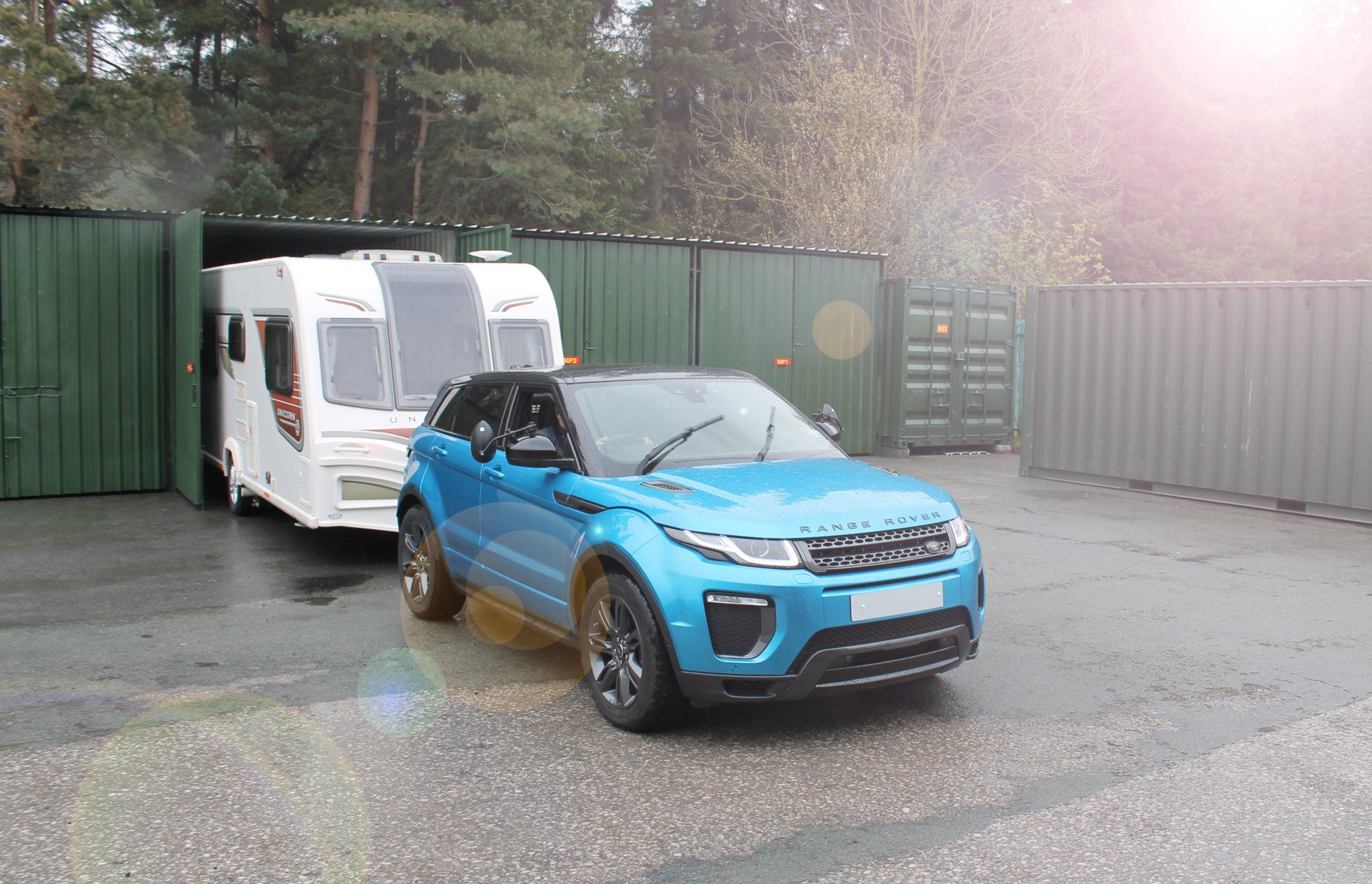 Blue SUV parked beside a white van in a wet industrial lot