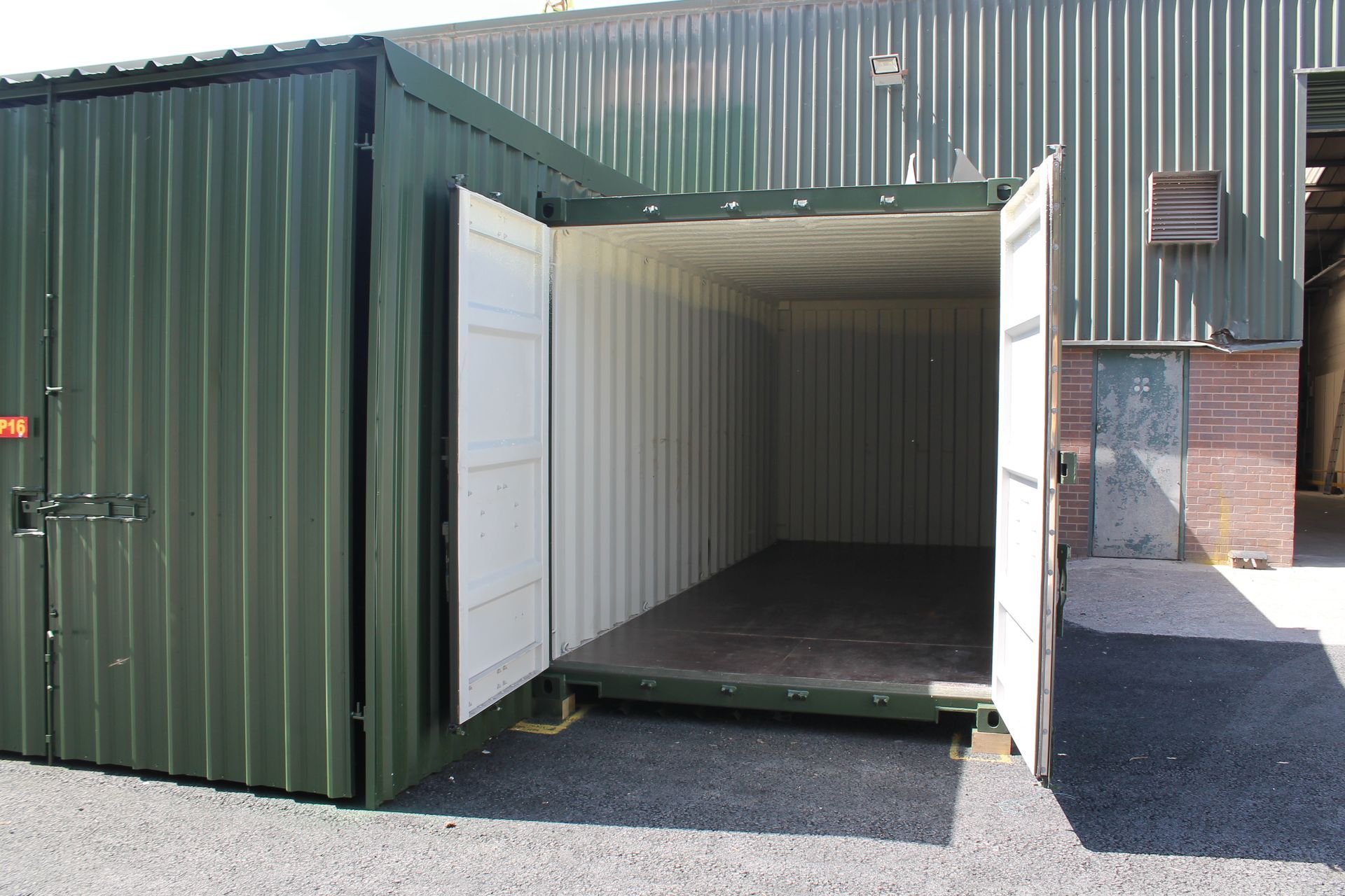 Open green shipping container with white double doors, showing an empty interior on a gravel lot.