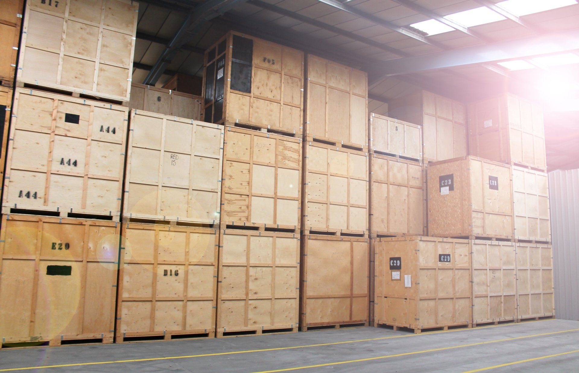 Stacked wooden shipping crates in a warehouse, numbered and arranged in rows under bright lights.