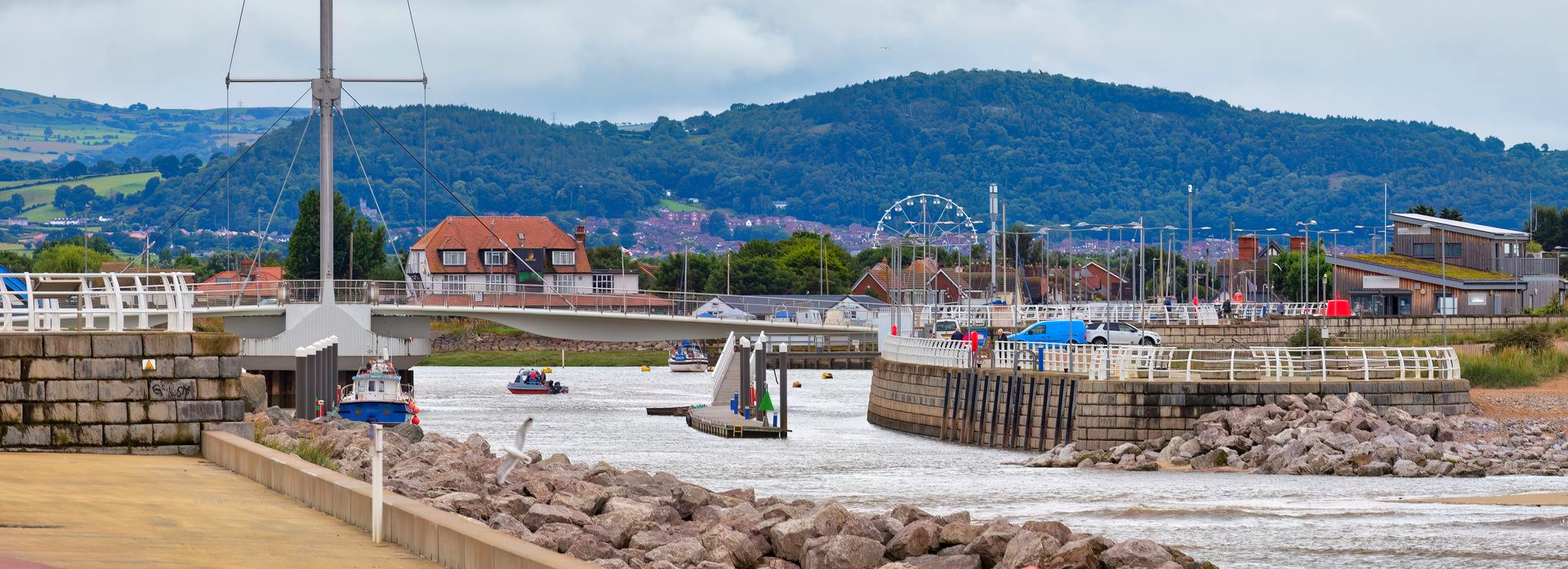 Rhyl Harbour, Wales with a rocky shoreline and wooden docks, white boats, and colourful houses under a cloudy sky