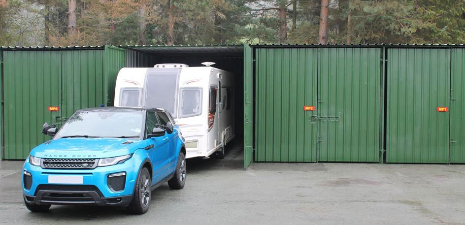 A blue car pulls a white caravan from within a green Arthur Owen Removals & Storage vehicle container with the doors open.