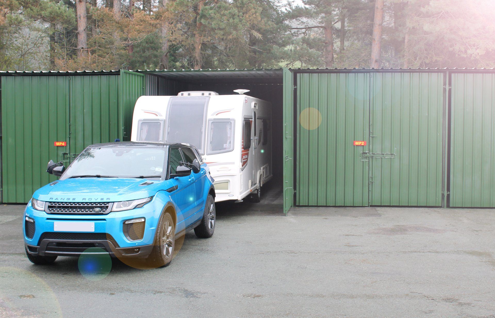 A blue SUV towing a white caravan from a green container storage unit from Arthur Owen Removals & Storage.