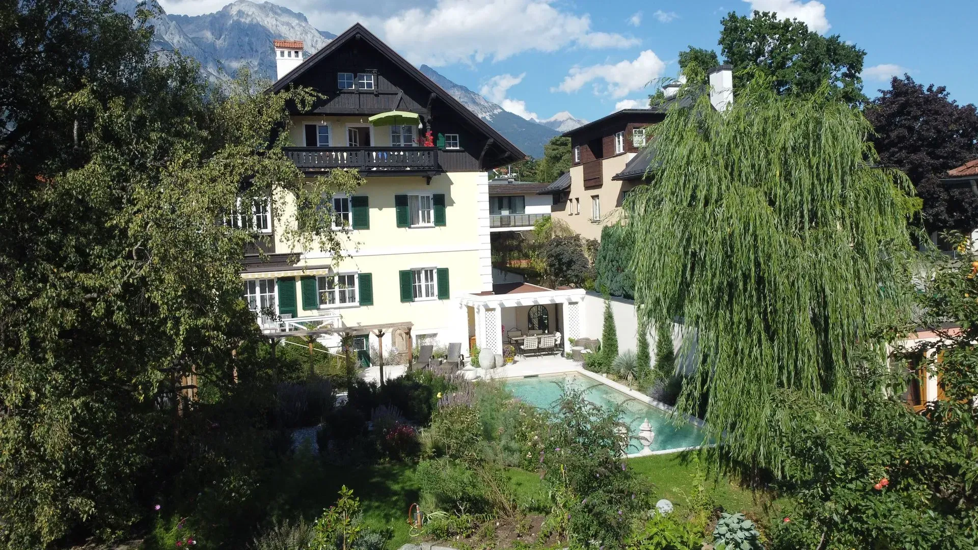 Charmantes Haus mit grünen Fensterläden und Pool, umgeben von üppigen Bäumen und Bergen.
