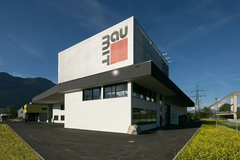 Modernes weißes Gebäude mit einem großen MOU-Schild, dunklem Dach und gepflegter Außenanlage unter blauem Himmel