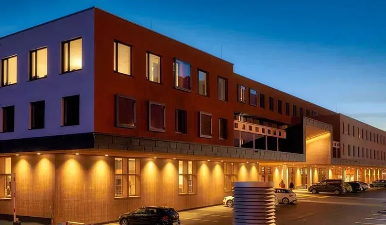 Modernes, mehrstöckiges Backsteingebäude in der Abenddämmerung mit erleuchteten Fenstern