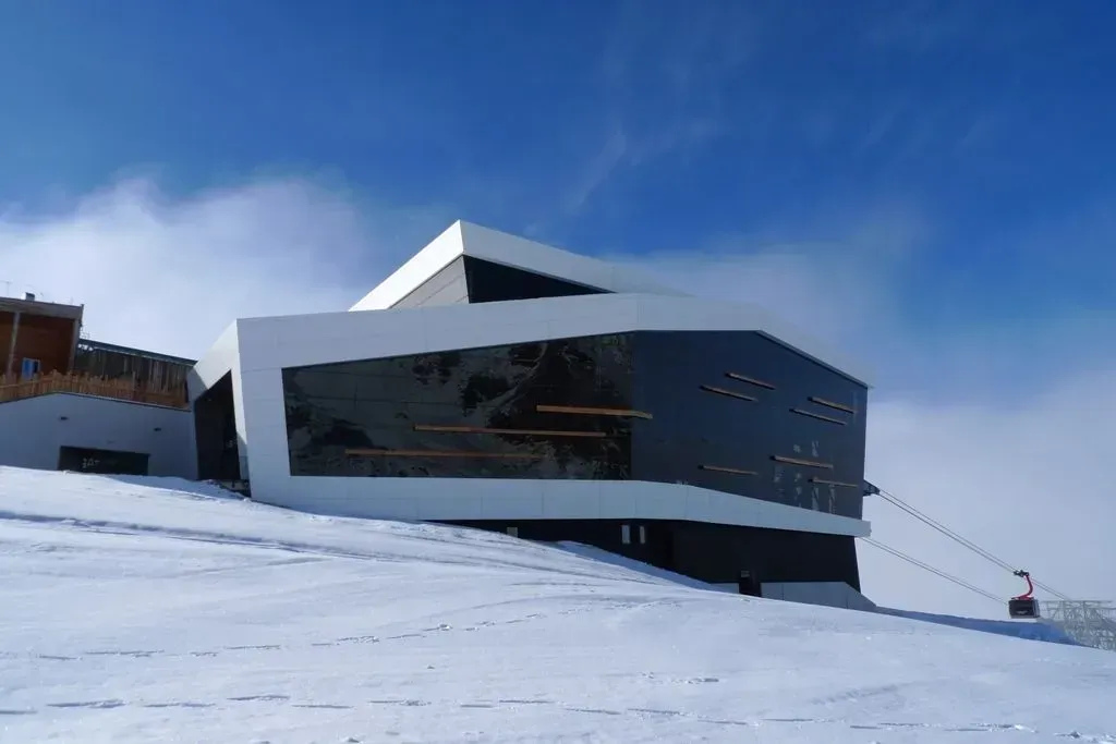 Modernes, kantiges Gebäude an einem schneebedeckten Hang unter blauem Himmel