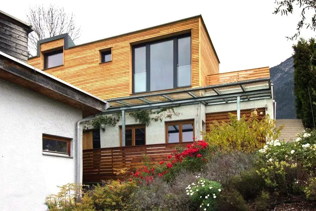 Modernes Haus mit Holzverkleidung, großen Fenstern und Garten am Hang