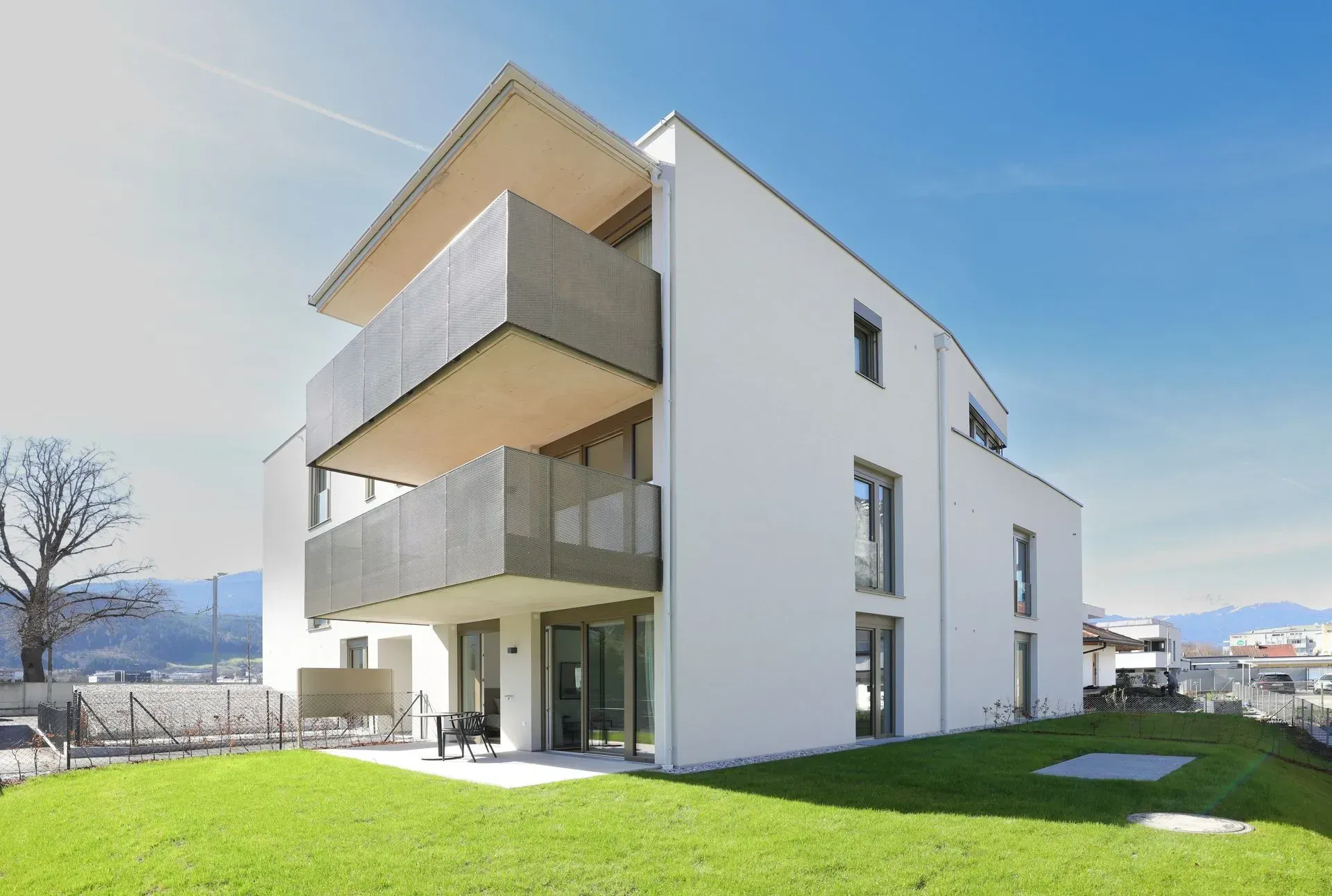 Modernes weißes Apartmentgebäude mit Balkonen und grünem Rasen unter klarem Himmel