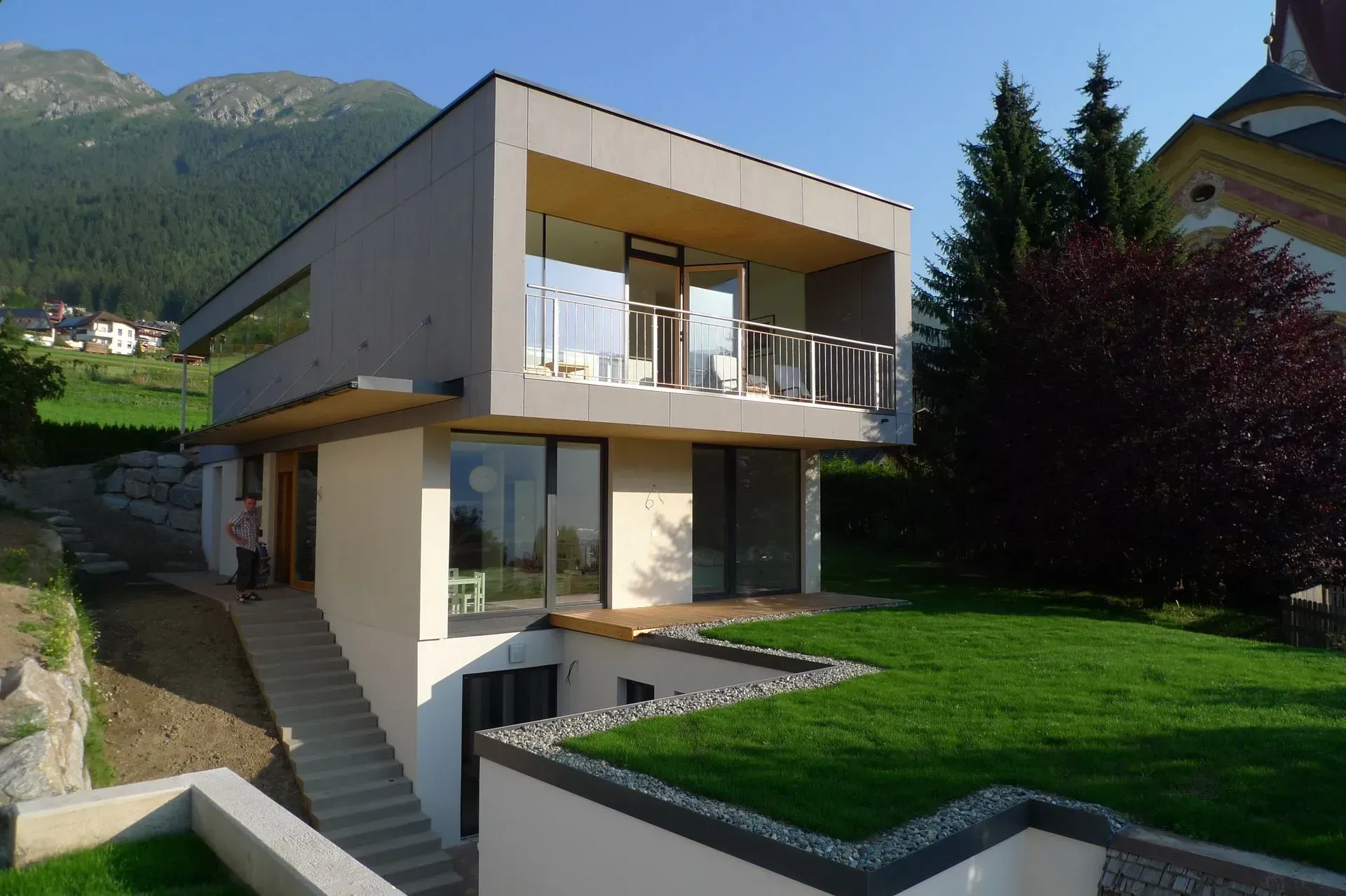 Modernes zweistöckiges Haus mit großen Fenstern, Balkonen und grünem Rasen in Berglage