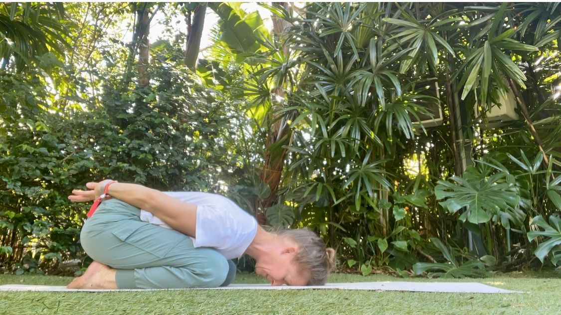 A woman is doing a yoga pose on a mat in the woods.