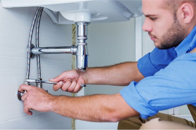 Plumber tightening pipe connections under a sink with a wrench in a kitchen cabinet