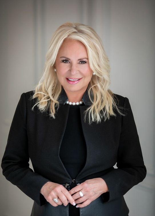 A woman is wearing a black jacket and a pearl necklace.