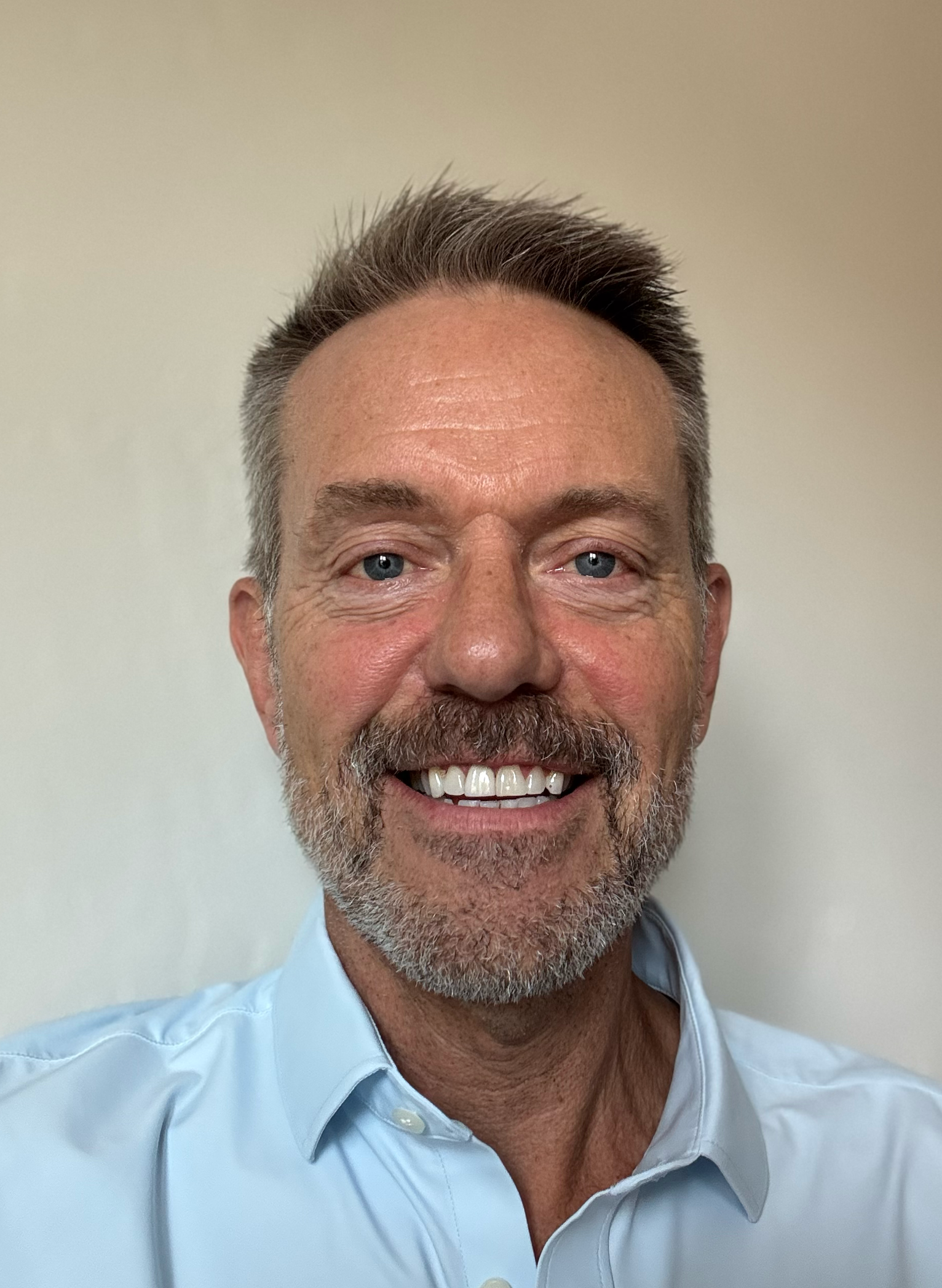 A man with a beard and a blue shirt is smiling for the camera.