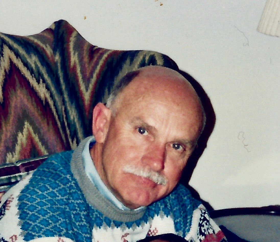 A bald man with a mustache is sitting in a chair
