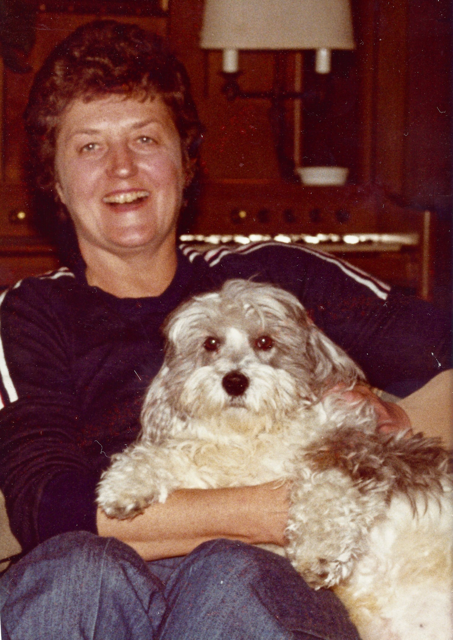 A woman is sitting on a couch holding a small dog.
