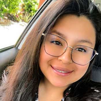 A woman wearing glasses is smiling while sitting in a car.