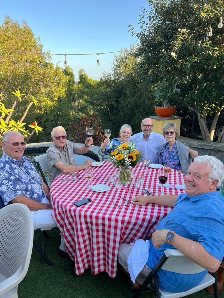 A group of people are sitting around a table with a red and white checkered tablecloth.