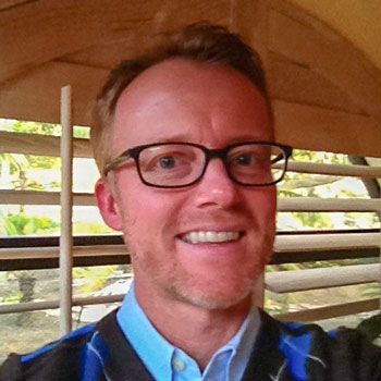 A man wearing glasses and a blue shirt is smiling for the camera.