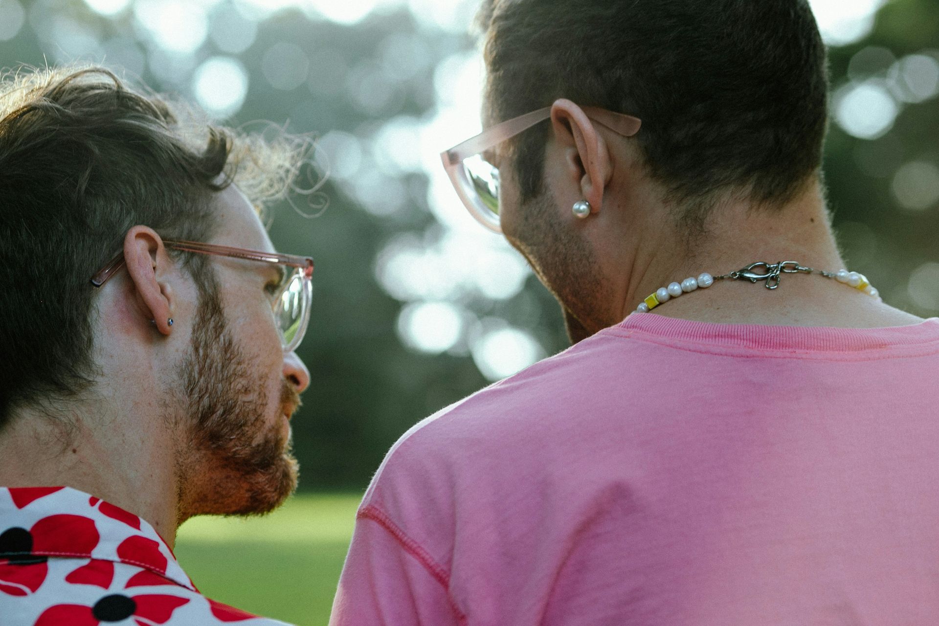 Two men are standing next to each other and looking at each other . one of the men is wearing a pink shirt.