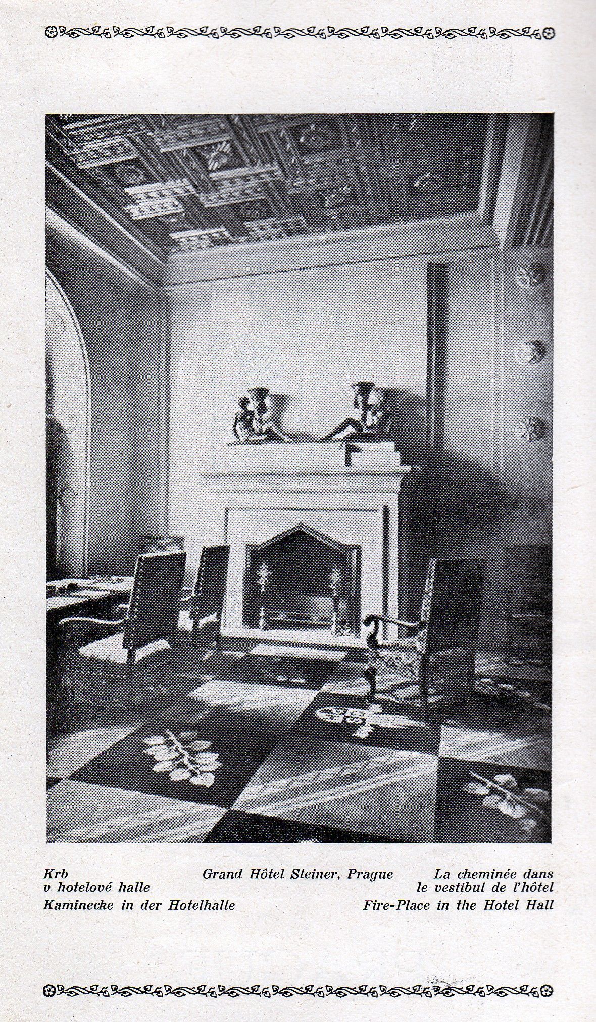 Two cats sit on a white mantel in a small room with a fireplace, a lamp, and patterned wallpaper.